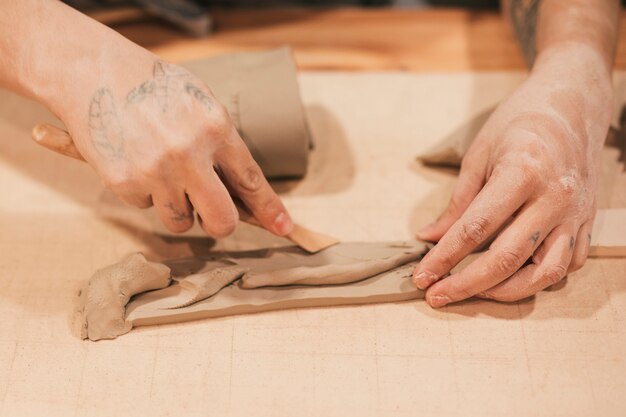 木製の道具で湿った粘土を成形する女性の陶工の手のクローズアップ