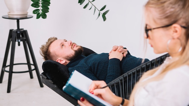 Foto gratuita primo piano dello psicologo femminile che annota le note durante la terapia con il suo paziente maschio