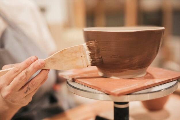 Close-up of female's hand applying the brown paint on bowl with paintbrush