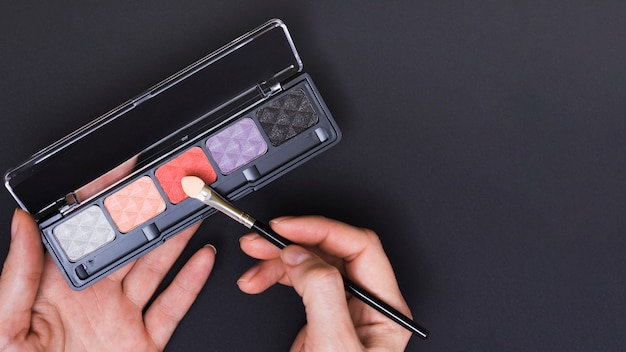 Close-up of female's hand applying the eyeshadow on black background