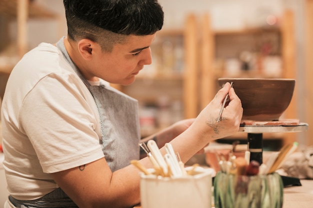 Free photo close-up of female's hand painting on the ceramic bowl with tools