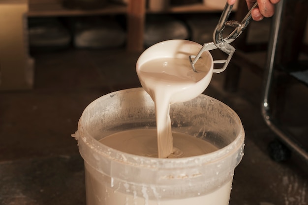 Free photo close-up of female's hand pouring paint with ceramic bowl in bucket