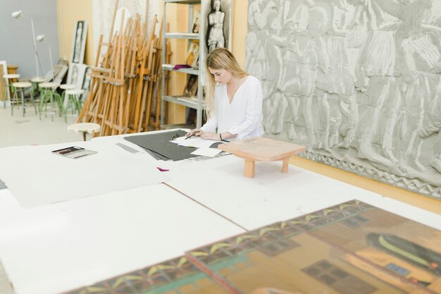 Close-up of female sketching on workbench over the table