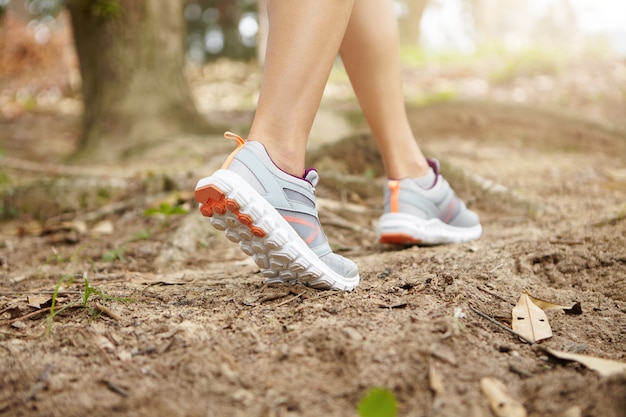 Close up of fit legs of young athletic woman wearing running shoes while running on forest trail. Rear view of female runner exercising outdoors, preparing for serious marathon.