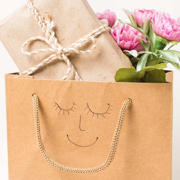 Close-up of flower bouquet and wrapped gift box in paper bag with hand drawn face on it