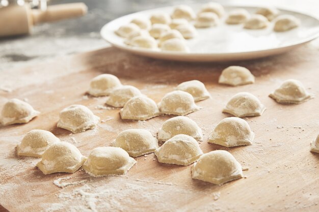 Close up focus ready tasty raviolis or dumplings filled with minced meat on flour on wooden board