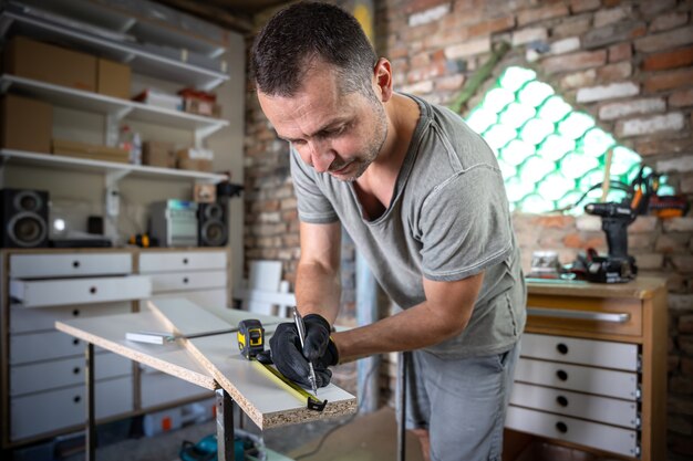 Close up of focused carpenter holding ruler and pencil while making marks on the wood at the table in the workshop.