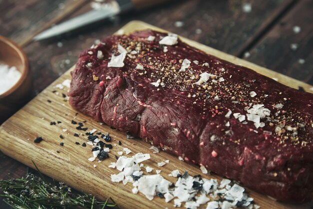 Close up focused piece of meat salted peppered on wooden board on vintage table between spices