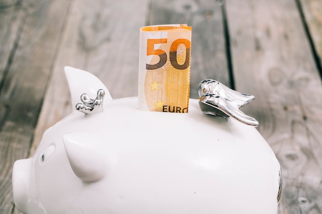 Close-up of folded fifty euro note in the slot of white piggybank