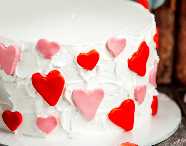 Close up of fondant hearts in red and pink on white creamy cake