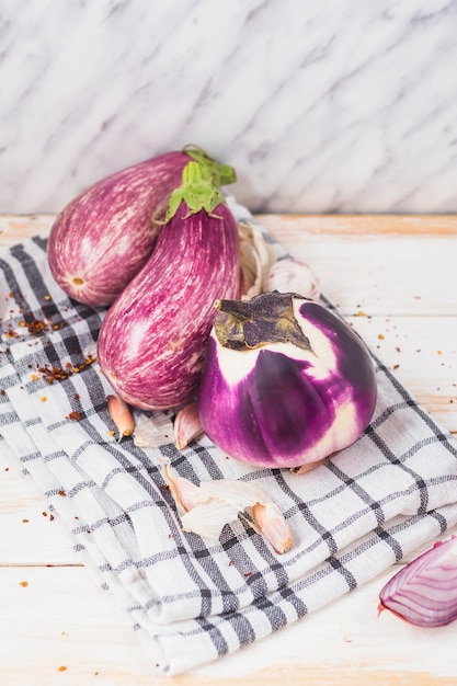 Close-up of fresh eggplants; onion; garlic cloves; chili flake and cloth on wooden tabletop