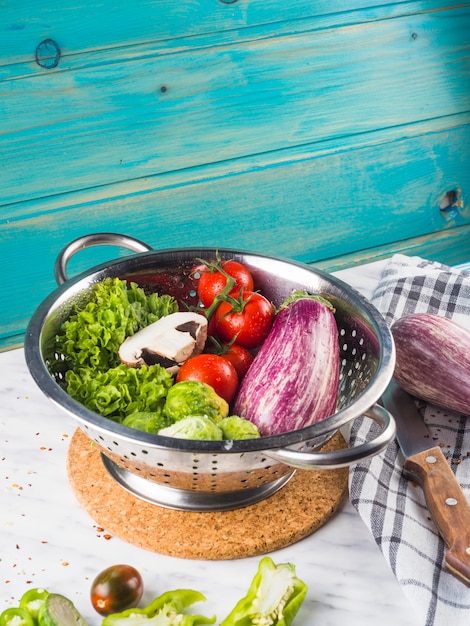 Close-up of fresh healthy vegetables in colander over marble desk