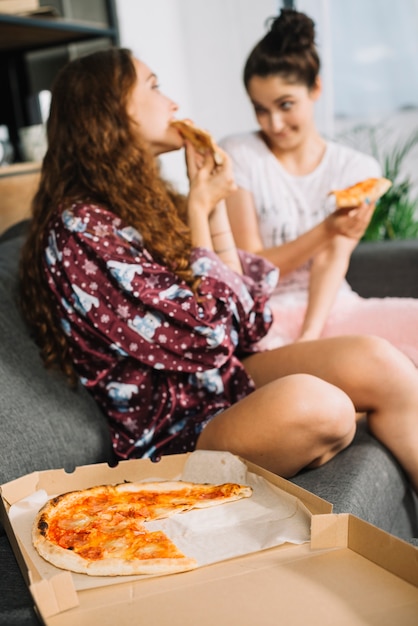 Close-up of fresh pizza in front of two women sitting on sofa