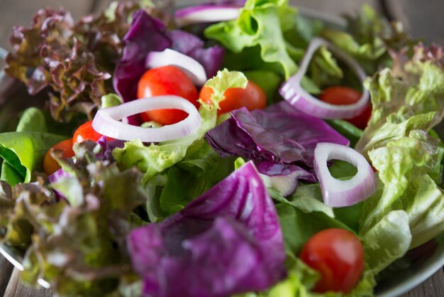 素朴な古い木製の背景とボウルで新鮮な野菜サラダのを閉じます。健康的な食べ物の概念。