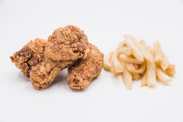 Close-up of fried chicken drumstick with french fries on white backdrop