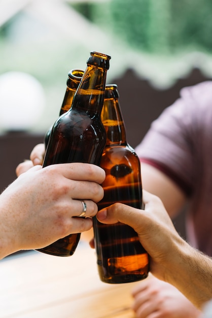 Close-up of friends clinking with brown bottles