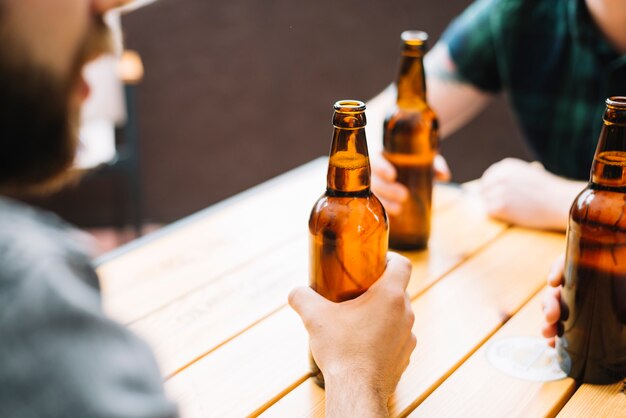 Close-up of friends holding beer bottles on wooden table
