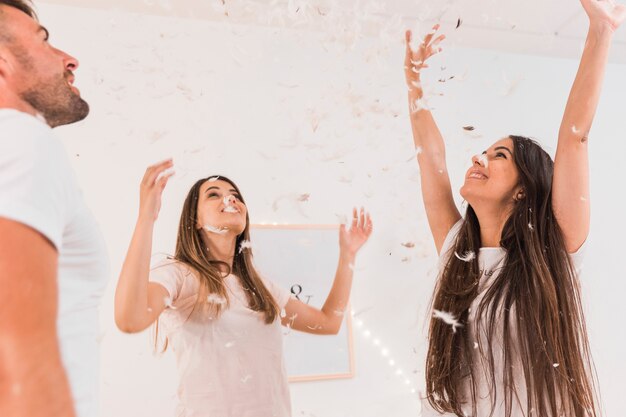 Free photo close-up of friends throwing white feather in air