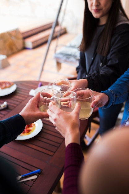 Close-up of friends toasting drink over wooden table