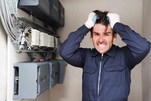 Close-up of frustrated male electrician standing near electric board