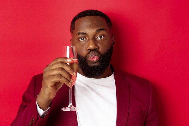 Close-up of funny Black man tasting champagne from glass, looking silly and pucker lips