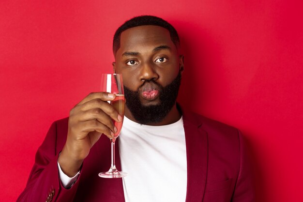 Крупный план смешного темнокожего мужчины, дегустирующего шампанское из стекла, выглядящего глупо и сморщившего губы