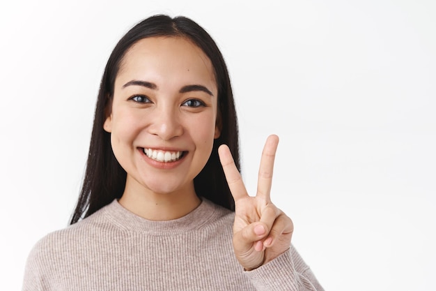 Close-up funny and enthusiastic, good-looking asian female 20s, showing peace gesture and smiling toothy, staying positive, leave positive feedback Premium Photo