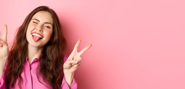 Free photo close up of funny and happy young woman having fun winking and showing tongue making vsign peace ges