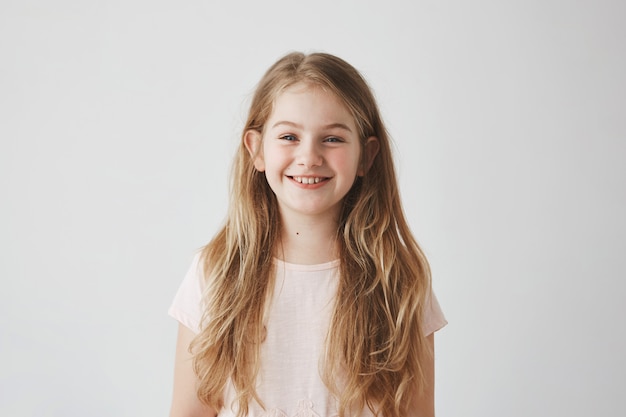 Close up of funny little girl with blue eyes and blonde hair laughing,  with satisfied expression, posing for family photo.