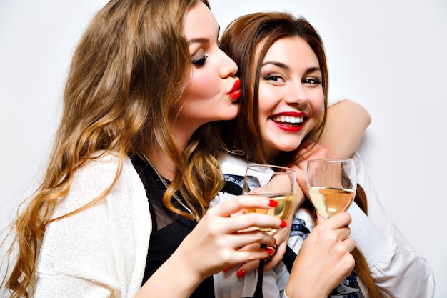 Close up funny portrait of pretty girls having fun on amazing party, bright make up, long hairs, holding glasses with champagne, pretty portrait of best friends, image with flash.