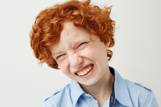 Chiuda in su del ragazzo dai capelli rossi divertente con le lentiggini che sorride con gli occhi chiusi, facendo i fronti sciocchi