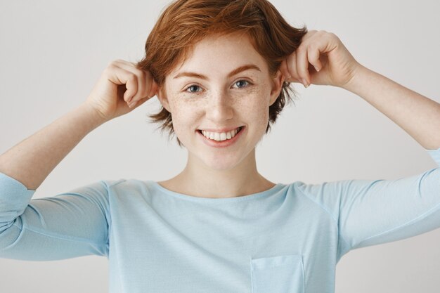 Close-up of funny and silly redhead girl posing against the white wall