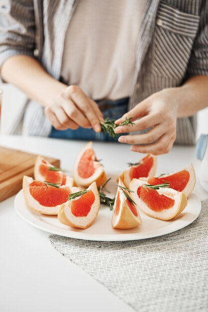 Close up of girl decorating plate with sliced grapefruit and rosemary. Fitness nutrition concept. Copy space.