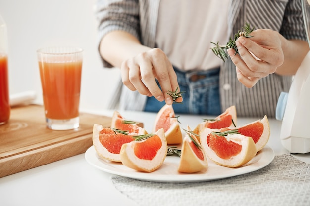 Close up of girl decorating plate with sliced grapefruit and rosemary. Fitness nutrition concept. Copy space.
