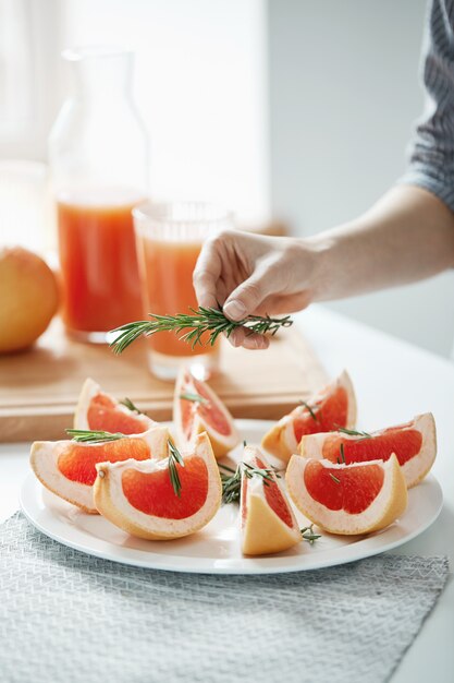 Close up of girl decorating plate with sliced grapefruit and rosemary. Fitness nutrition concept. Copy space.