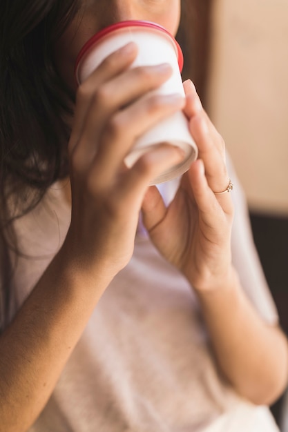 テイクアウトコーヒーカップからコーヒーを飲む女の子のクローズアップ