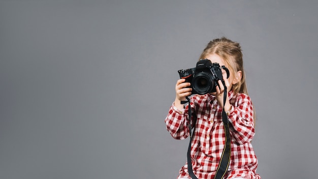 Крупным планом девушки с фотоаппаратом перед ее лицом, стоящим на сером фоне