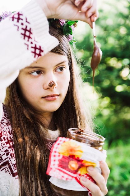 Close-up of a girl holding chocolate dripping from spoon in jar