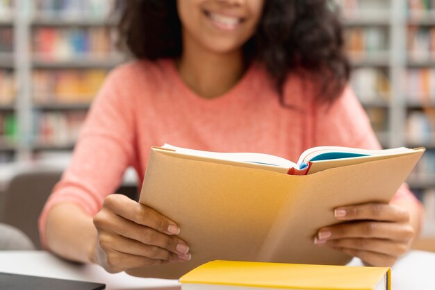 Девушка крупного плана на библиотеке изучая и используя компьтер-книжку