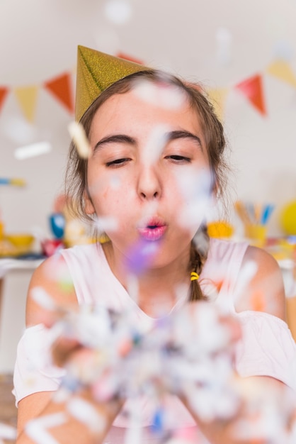 Foto gratuita primo piano della ragazza in cappello di partito che soffia coriandoli