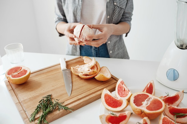Close up of girl peeling grapefruit over white wall. Healthy fitness nutrition concept.