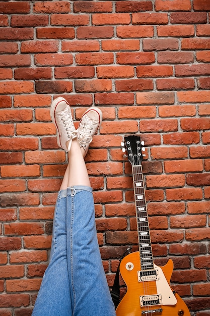 Foto gratuita chiuda in su dei piedini e della chitarra della ragazza sopra la priorità bassa del mattone.