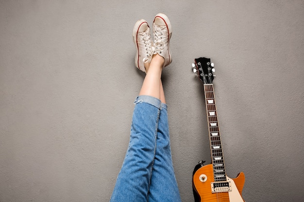Close up of girl's legs and guitar over grey background.