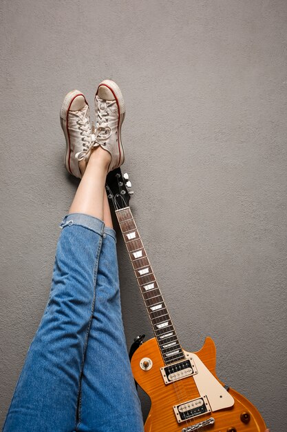 Close up of girl's legs and guitar over grey background.