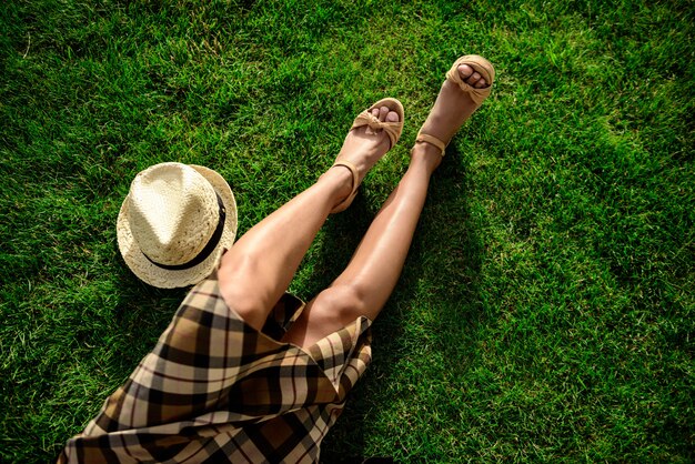 Close up of girl's legs and hat lying on grass.