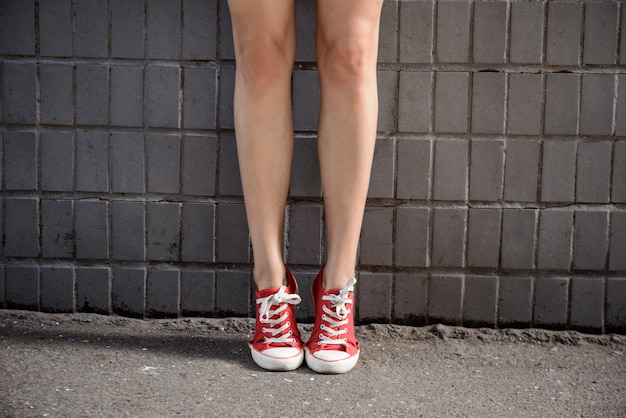 Free photo close up of girl's legs in keds over grey wall.