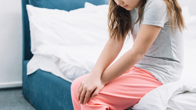 Close-up of a girl sitting on bed touching her knees with two hands