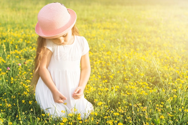 黄色の花を摘む草原に座っている女の子のクローズアップ