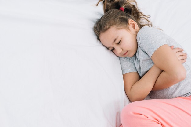 Close-up of a girl sleeping on white bed with pain