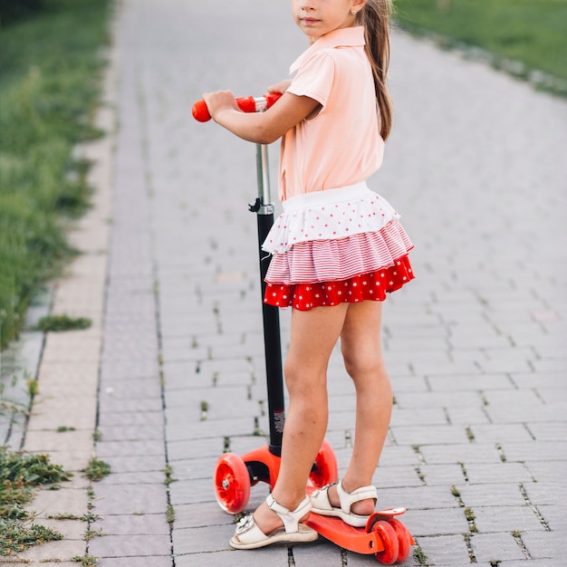 Close-up of a girl standing on push scooter in the park